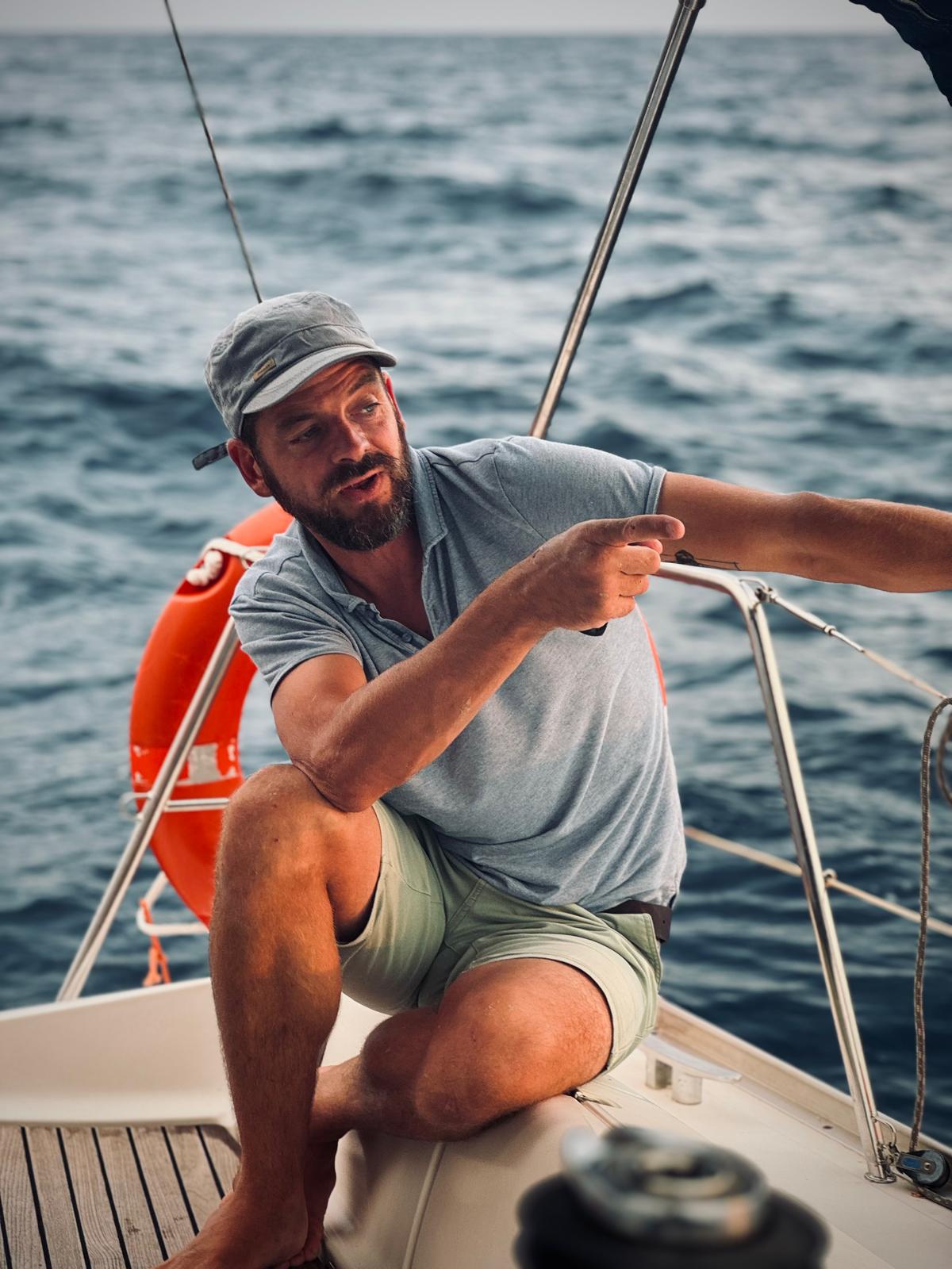 Jean, professional skipper of Sail Away Barcelona, pointing towards the horizon at sea